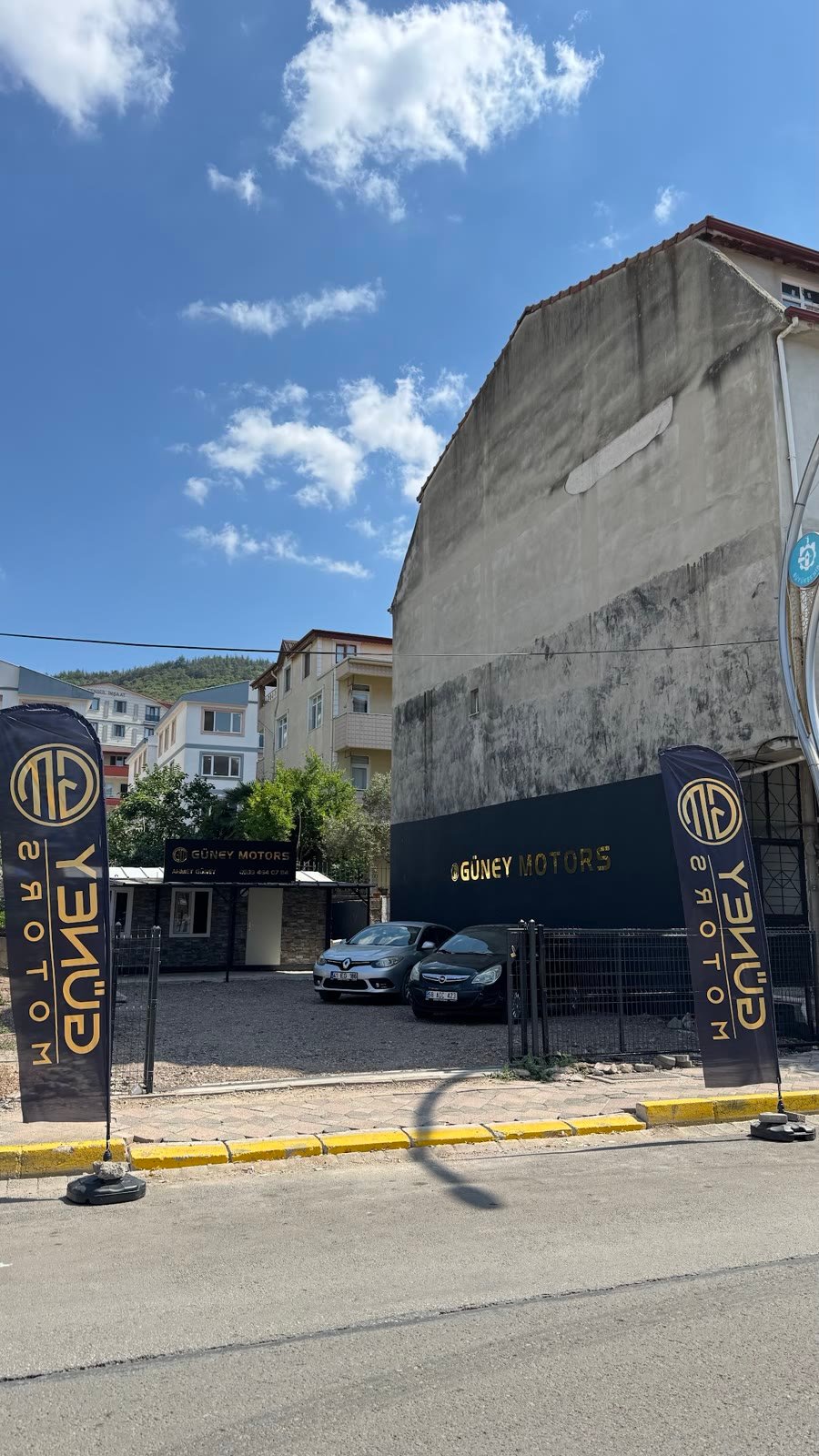 Güney Motors galeri girişi, altın logolu bayraklar ve ofis